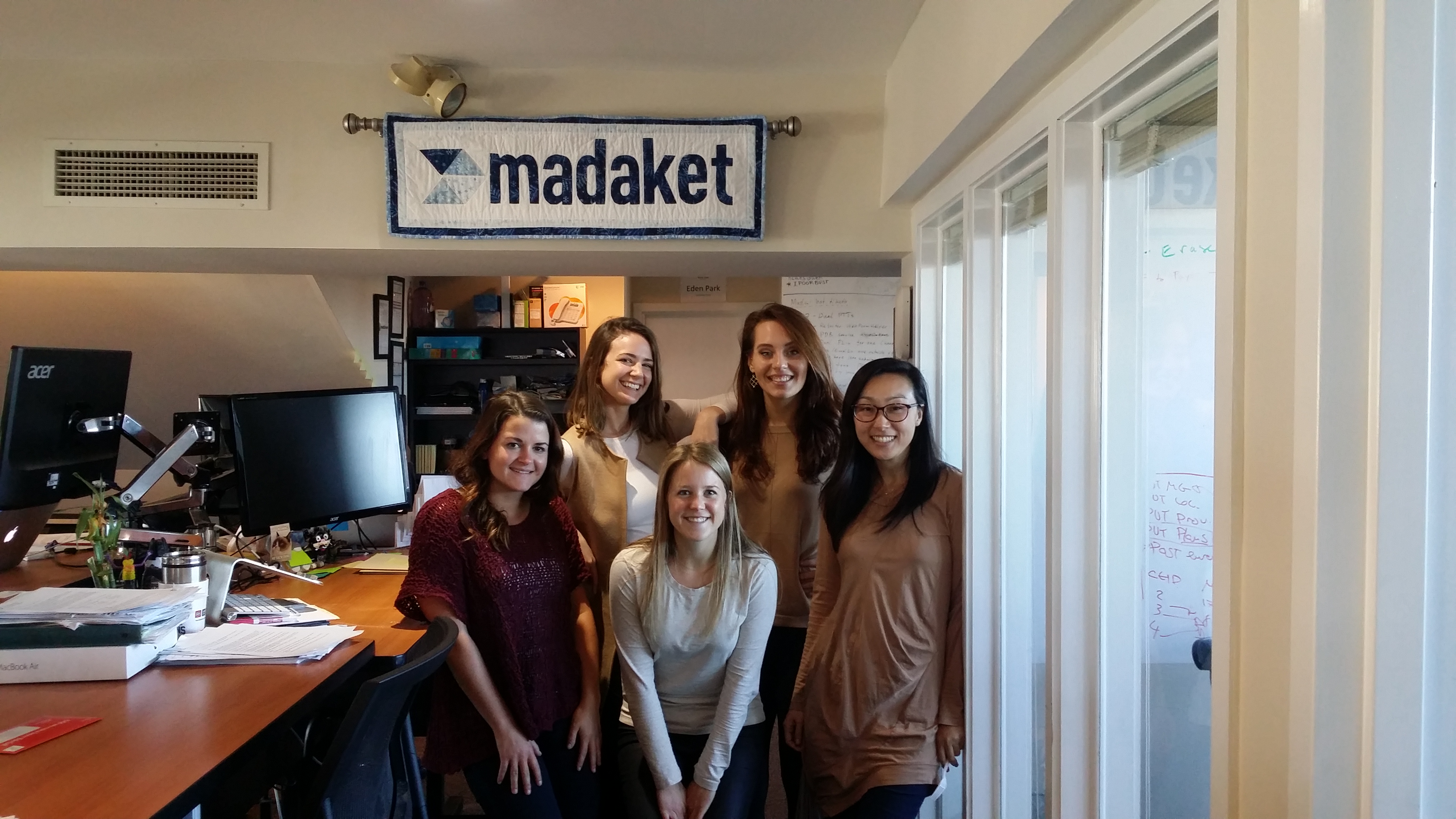 5 Madaket employees standing underneath The "Madaket quilt" hanging in the office