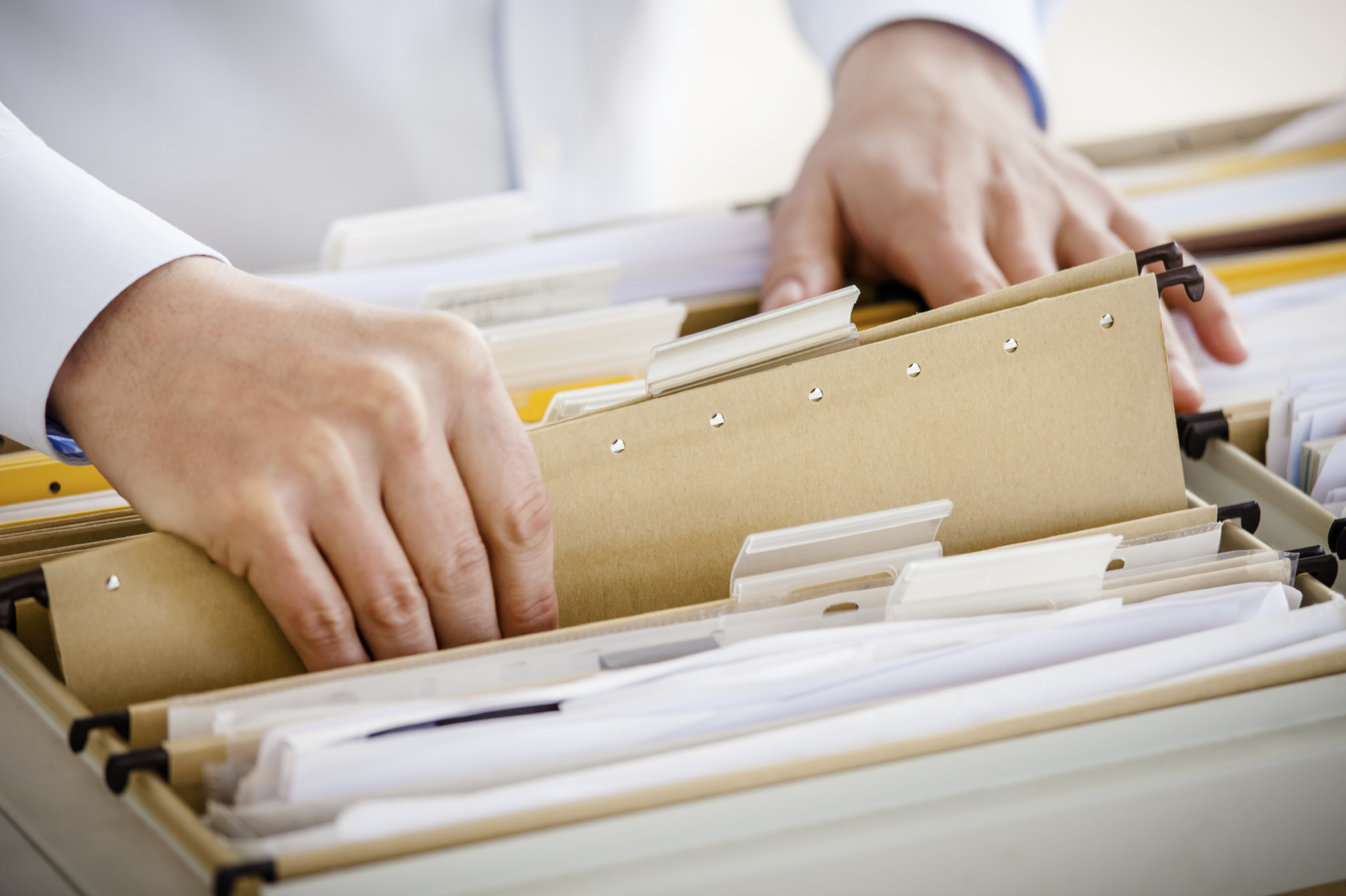 An individual sifting through a file cabinet of multiple manilla file folders